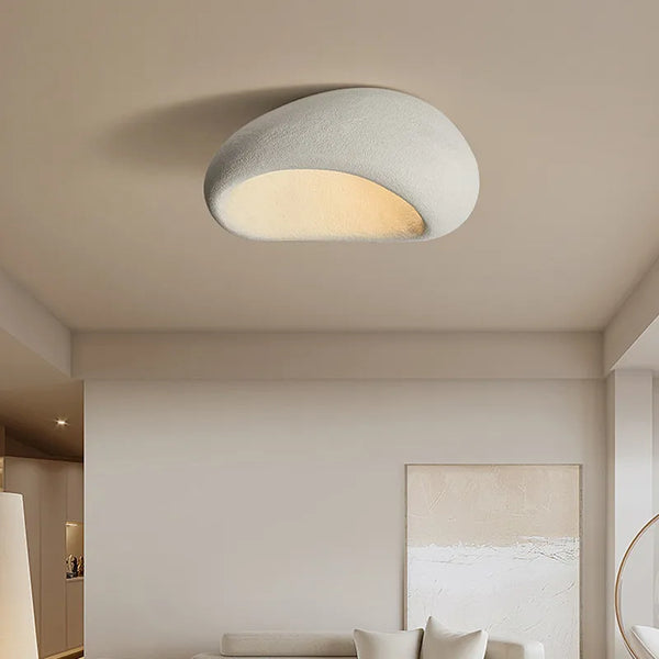 Vit wabi-sabi taklampa med stenliknande form i ett stilrent vardagsrum