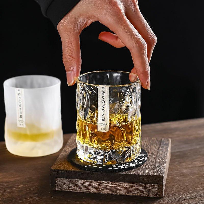 En hand lyfter ett japanskt Glacier whiskyglas på ett träunderlägg