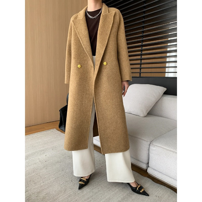 Dam bär lång dubbelknäppt kappa i färg camel med vida krage och svarta accessoarer