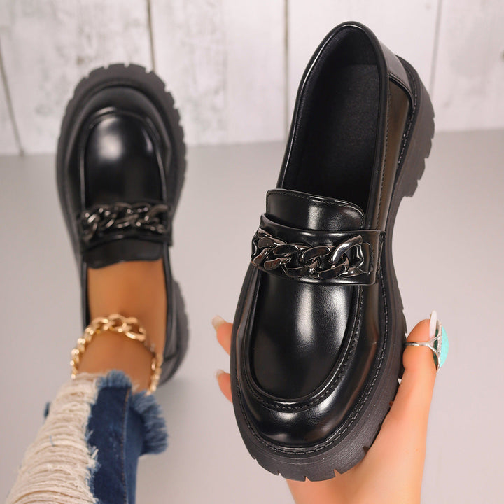 Närbild på svarta slip-on loafers med dekorativ kedja och kraftig sula