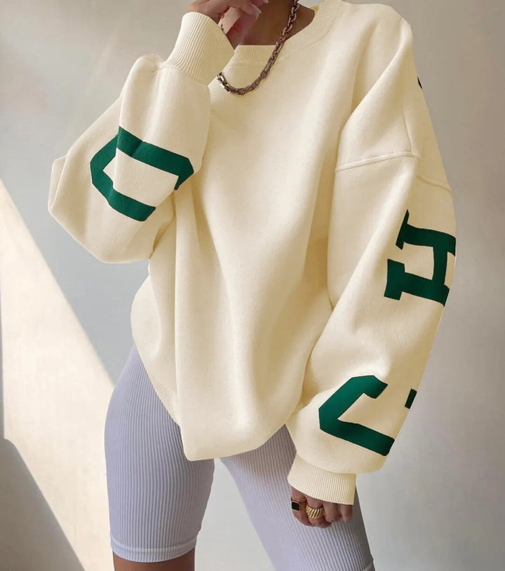 Kvinna i krämvit oversized sweatshirt med grönt tryck på ärmen