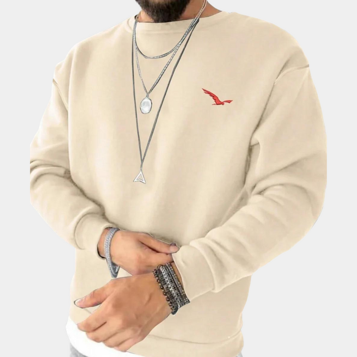 Närbild på beige tröja med diskret broderad detalj på bröstet