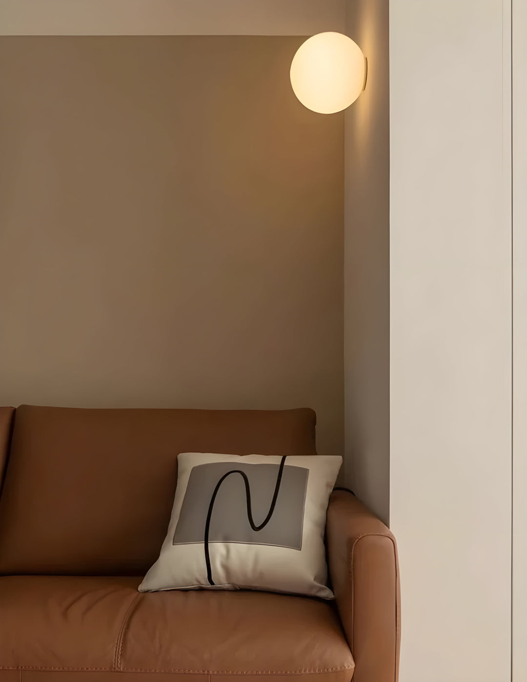 Rund glasvägglampa med varmt ljus monterad på beige vägg ovanför soffa
