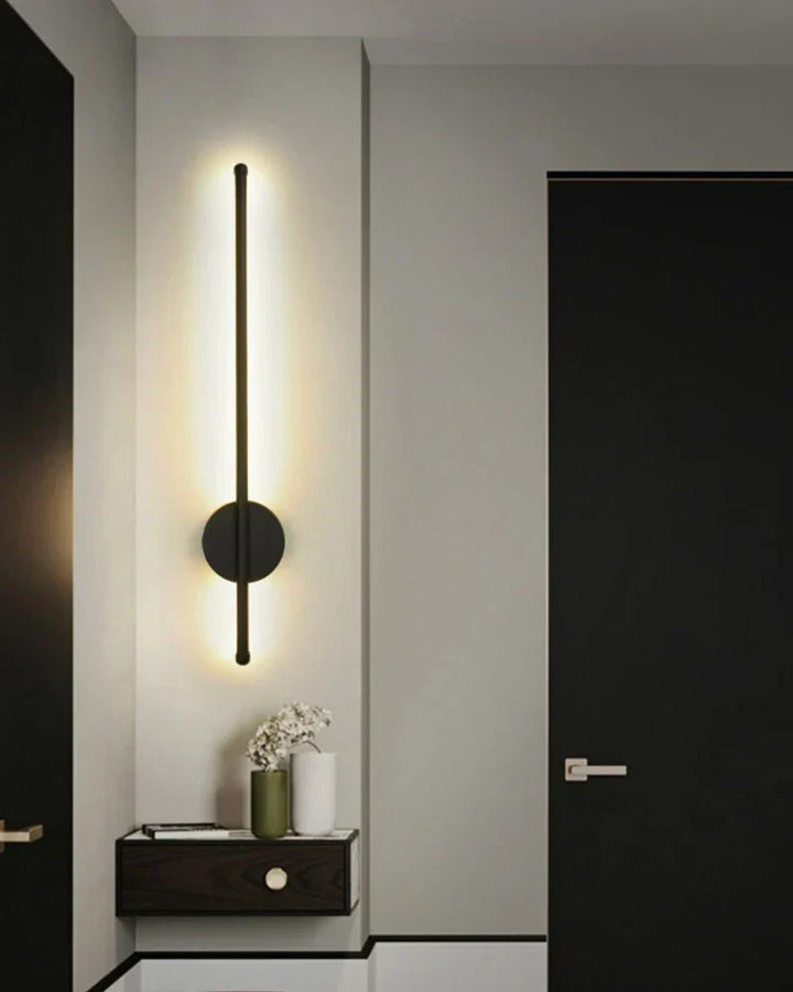 Svart lång LED vägglampa placerad vertikalt i en modern hallmiljö
