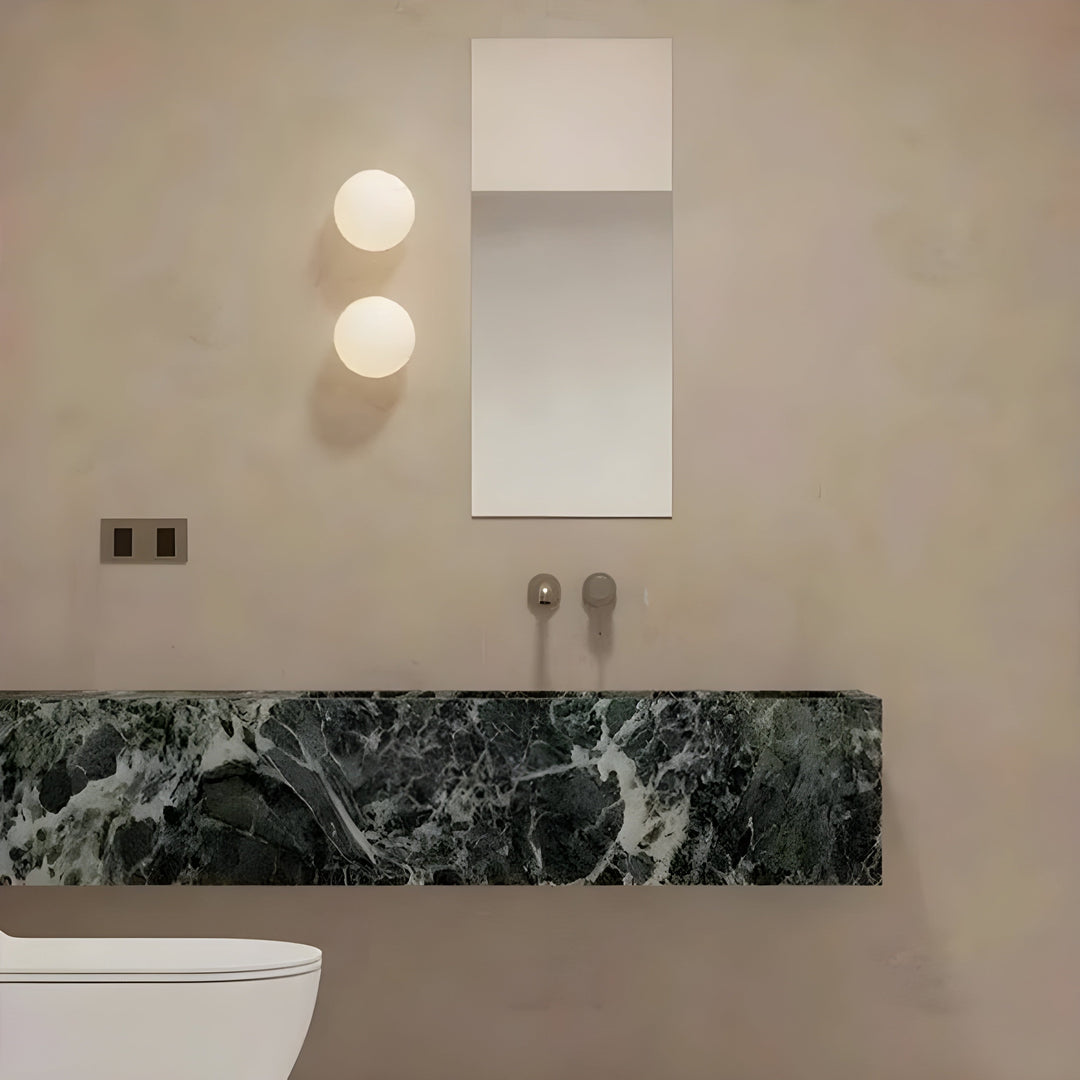 Två runda LED-vägglampor i glas placerade vertikalt bredvid spegel i badrum