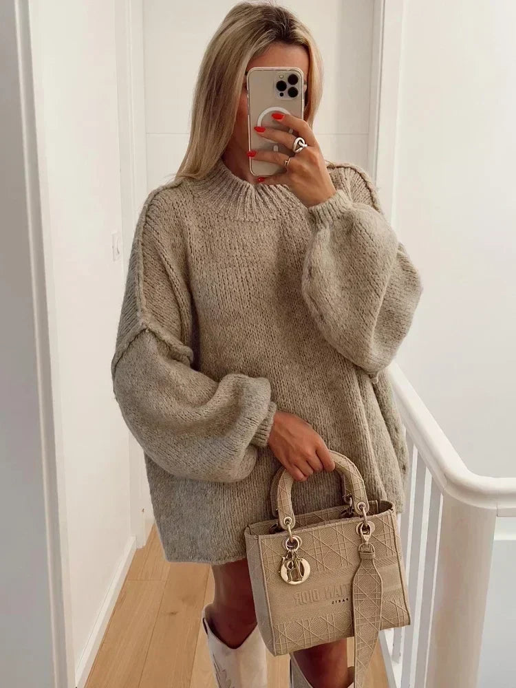 Kvinna i beige oversized stickad tröja med hög hals och ballongärm