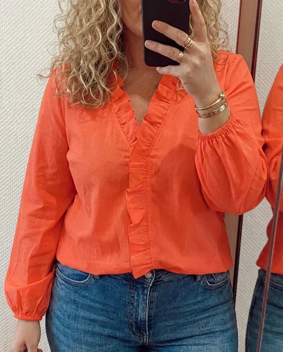 Kvinna i orange blus med volanger och jeans