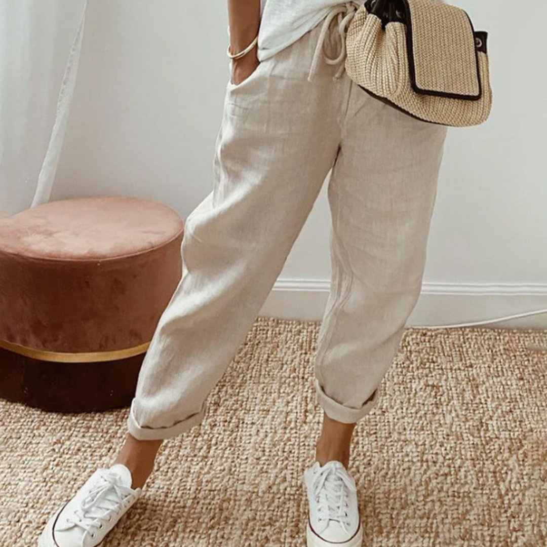 Kvinna i beige byxor med vit överdel och vita sneakers