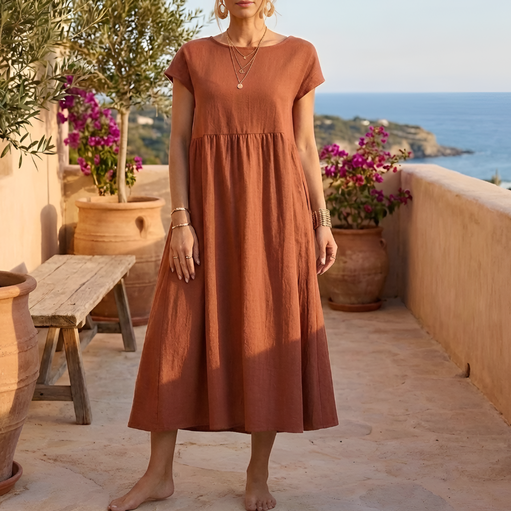 Kvinna i rödockra vintageklänning utomhus på terrass med olivträd