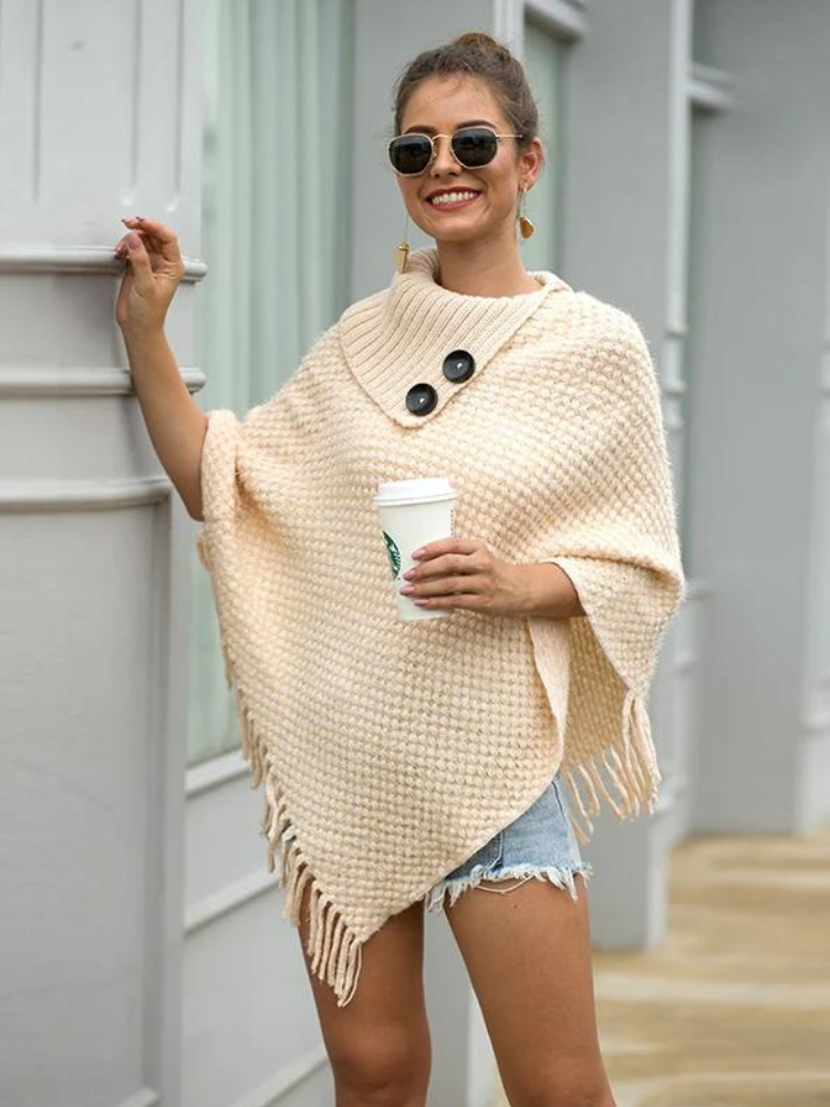 Kvinna i beige stickad poncho med solglasögon utomhus
