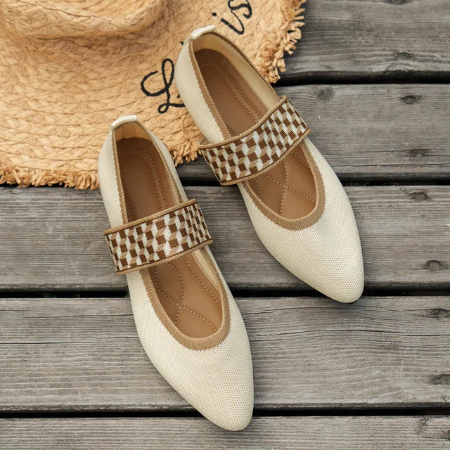 Ovanifrån på ett par eleganta beige damskor med mönstrad rem på träunderlag