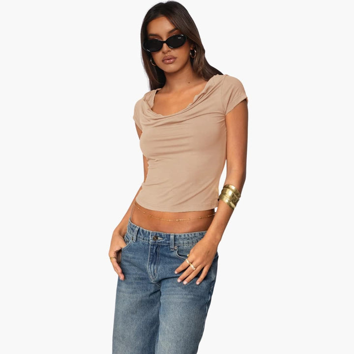 Kvinna i aprikosfärgad T-shirt med draperad vattenfallshals och jeans