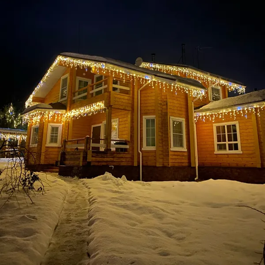 Trähus med varmvit LED-ljusgardin längs taket i snölandskap