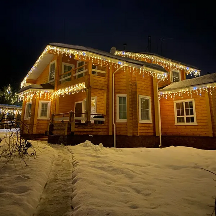 Trähus med varmvit LED-ljusgardin längs taket i snölandskap