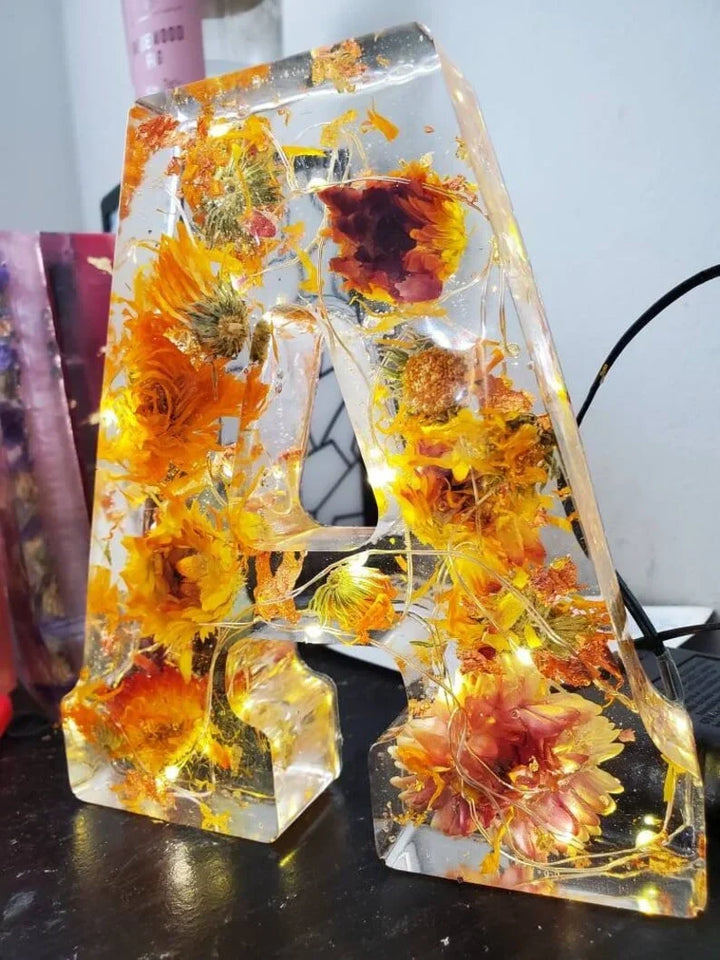 Närmast en gul och orange bokstavsformad harts-lampa med torkade blommor och LED-slinga.