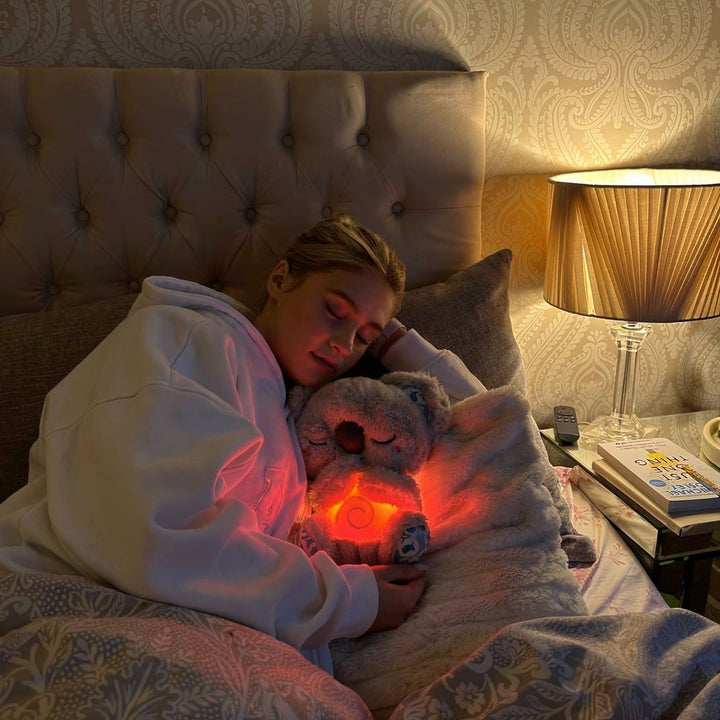 Kvinna som sover gott i sängen med en upplyst andande koala