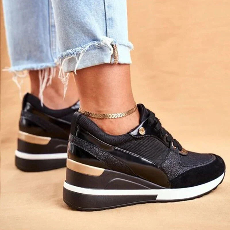 Sida av svarta sneakers med högre sula och gulddetaljer