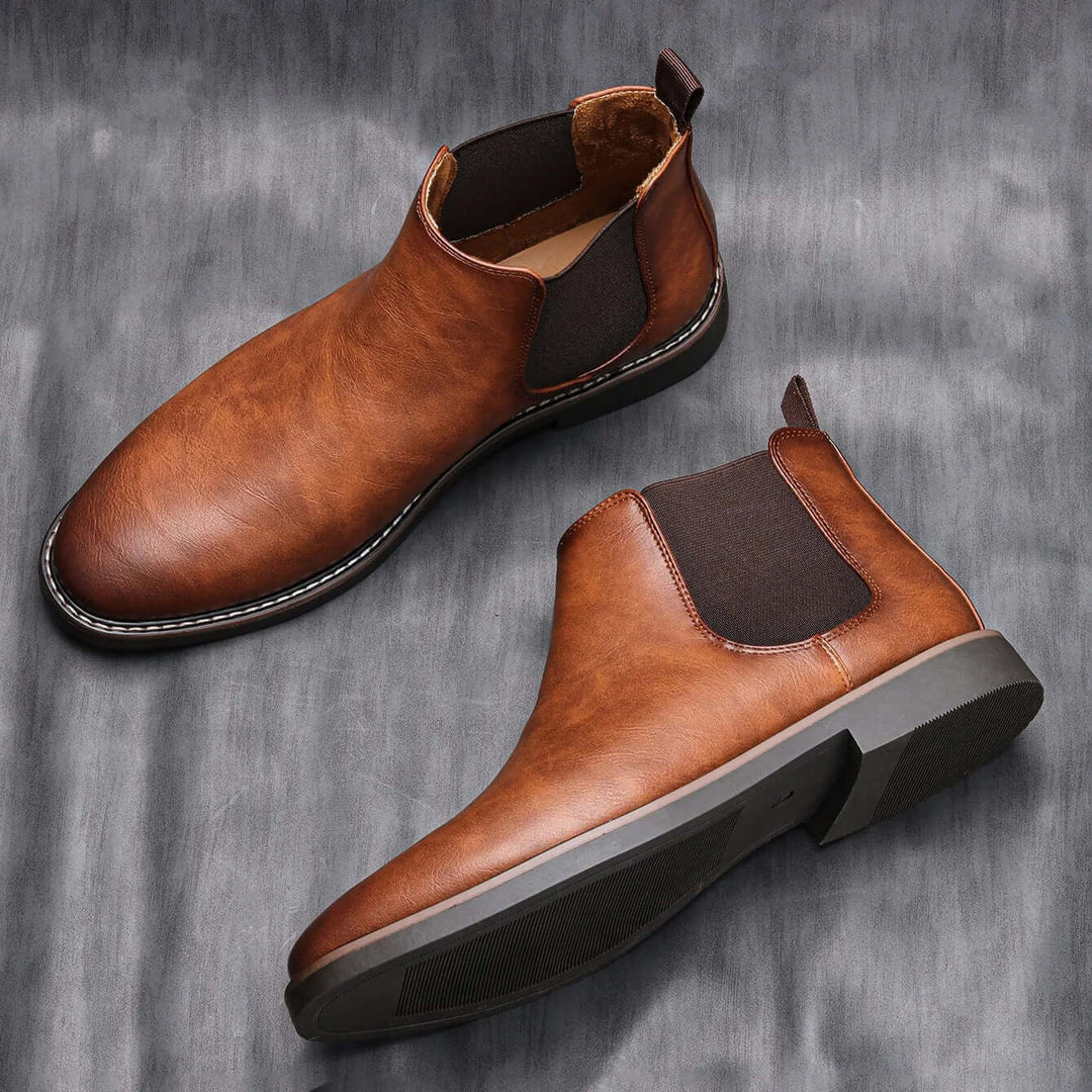 Två bruna chelsea boots fotograferade från vinkel med sula och häl