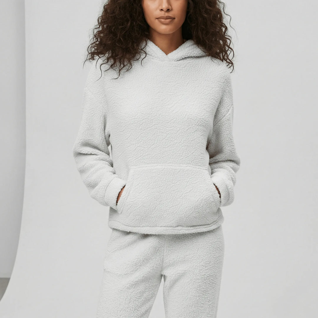 Kvinna bär mjukt dam loungewear-set med huva och känguruficka. Bekväma hemmakläder.