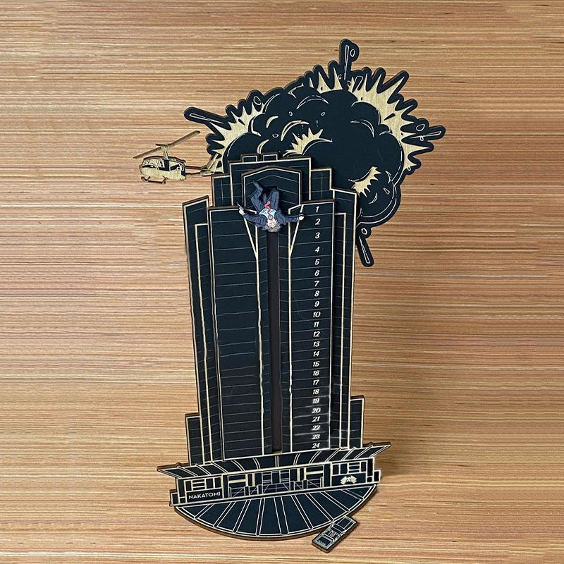 "Detaljerad trä Adventskalender med Die Hard-motiv, visar Hans Gruber faller från brunblå Nakatomi Plaza, roterbar design."