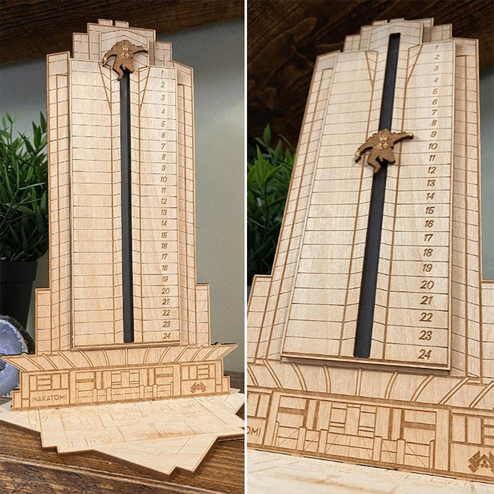 "Detaljerad trä Adventskalender med Die Hard-motiv, visar Hans Gruber faller från brunblå Nakatomi Plaza, roterbar design."