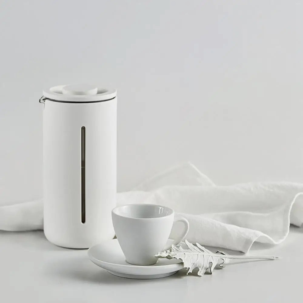 Vit fransk press kaffebryggare bredvid en kaffekopp på bord
