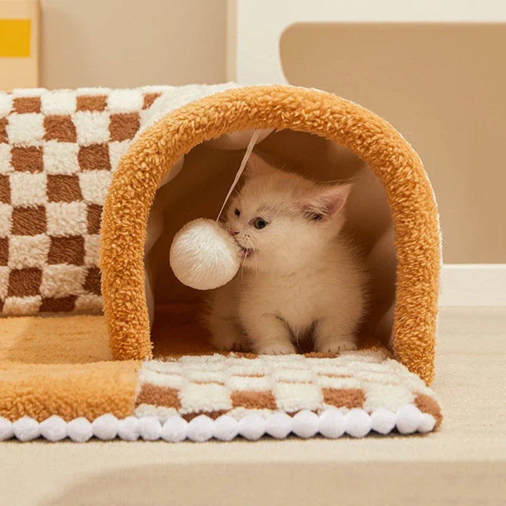 Kattunge som leker med en hängande boll inuti den mjuka plyschtunnelfållan
