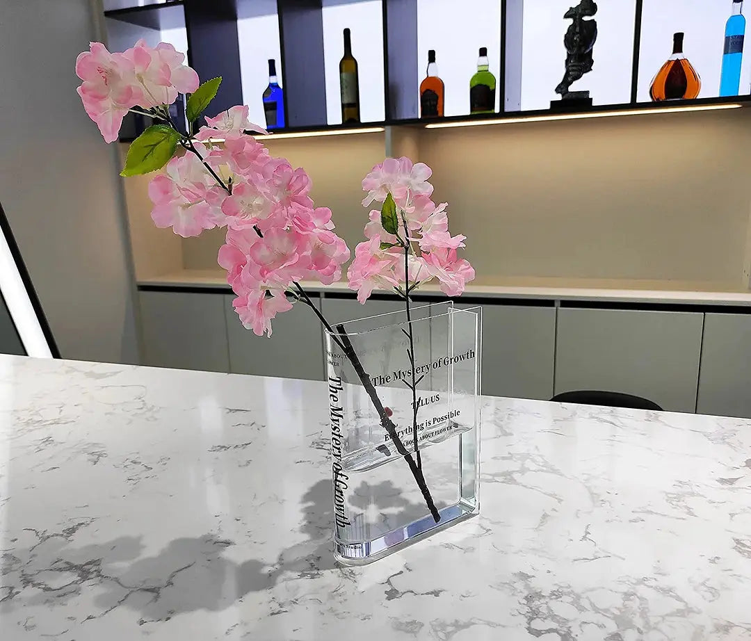 Akrylvas i bokform fylld med rosa blomsterarrangemang i modern miljö
