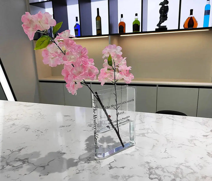 Akrylvas i bokform fylld med rosa blomsterarrangemang i modern miljö