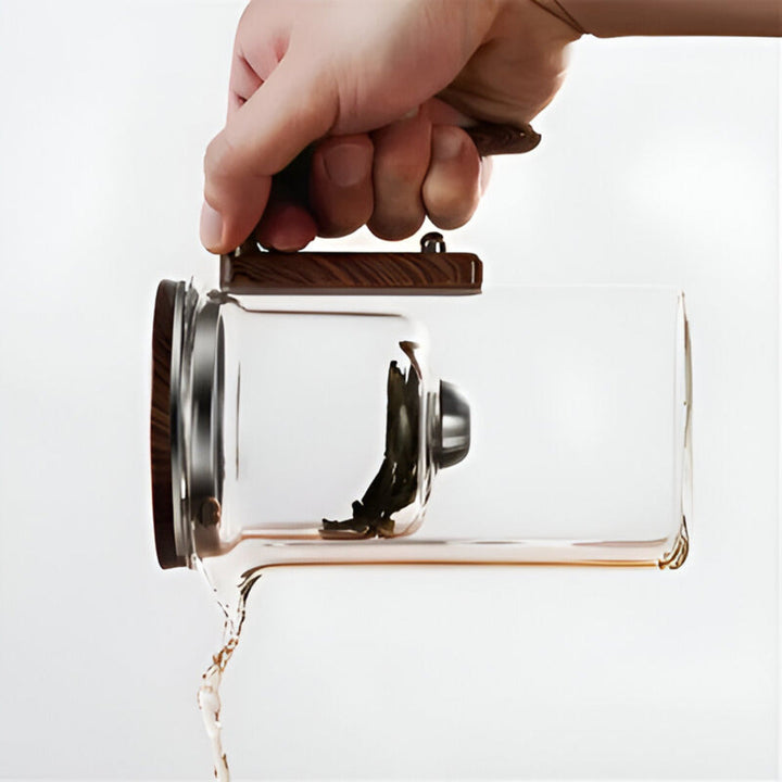 Designad glastekanna med ergonomiskt handtag och precisionspip för spillfri servering av te.