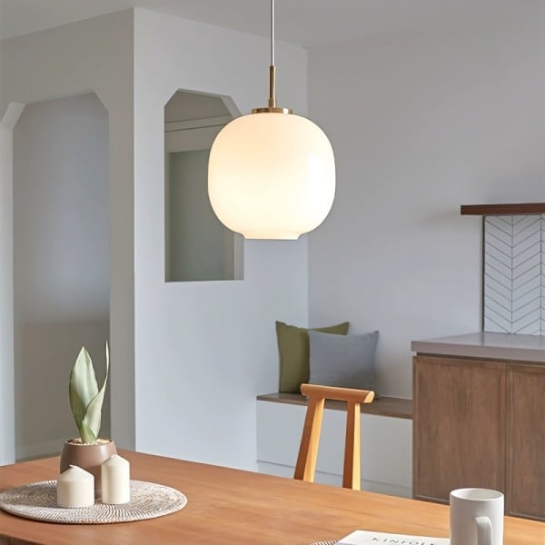 Modern taklampa i opalglas som hänger över ett träbord i ett ljust rum