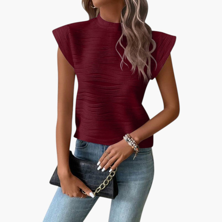 Modeinriktad ärmlös damtopp med hög krage. Texturerad yta ger elegant sommarlook.