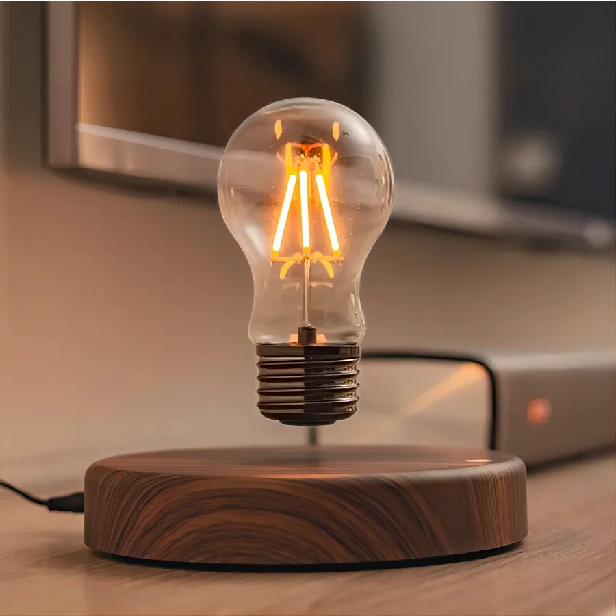 Magnetisk svävande LED-lampa med tänd glödlampa över träbas på skrivbord