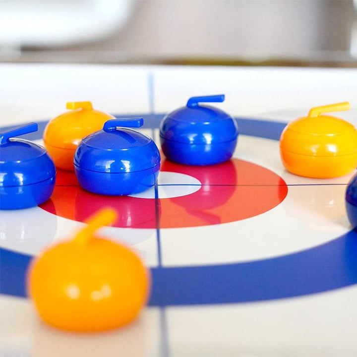"Familjevänligt bordscurlingspel med slät isliknande yta, uppställd spelplan och färgglada curlingstenar"