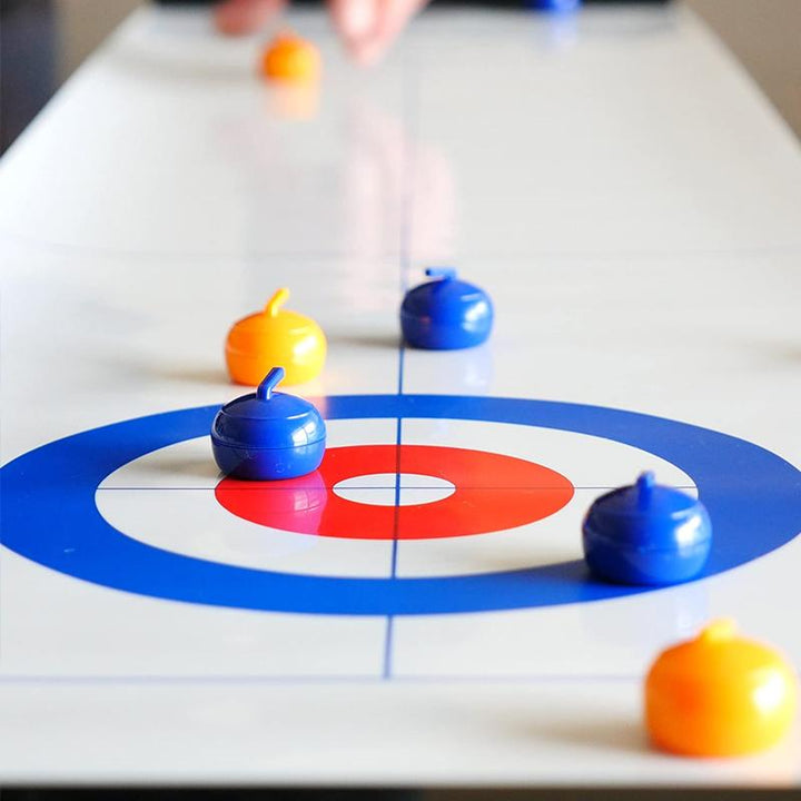 "Familjevänligt bordscurlingspel med slät isliknande yta, uppställd spelplan och färgglada curlingstenar"