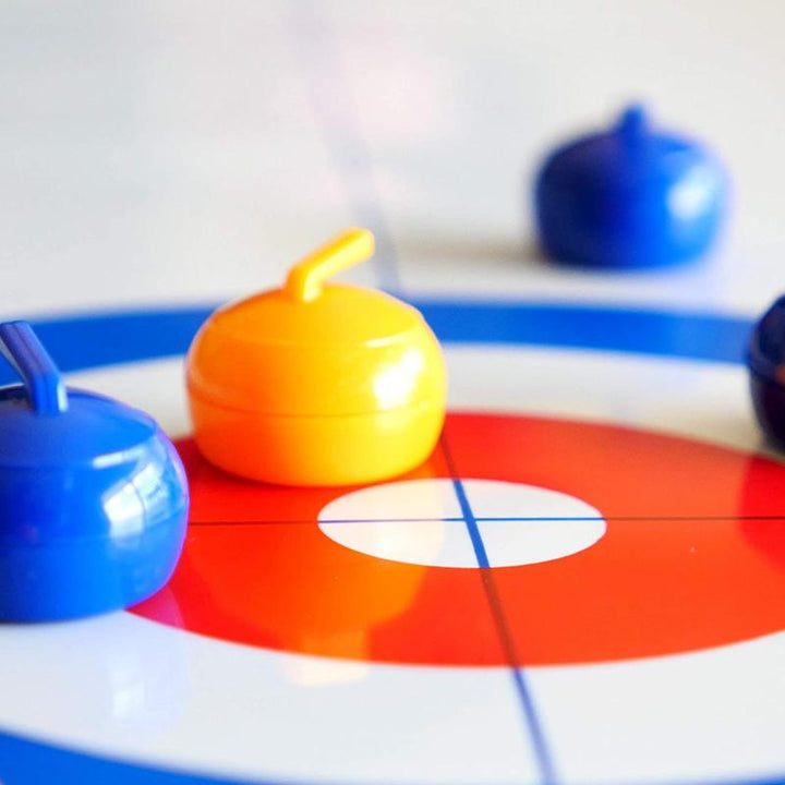 "Familjevänligt bordscurlingspel med slät isliknande yta, uppställd spelplan och färgglada curlingstenar"