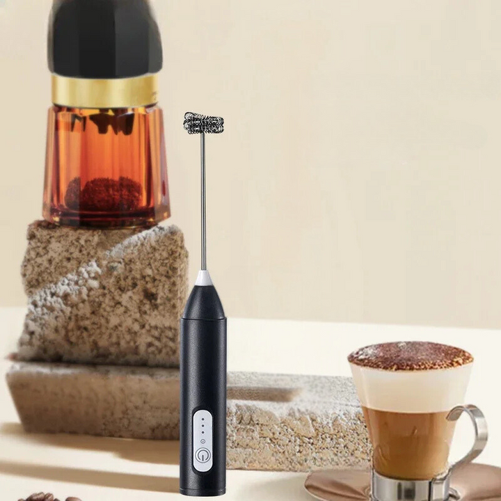 Svart elektrisk mjölkskummare placerad bredvid en kopp kaffe