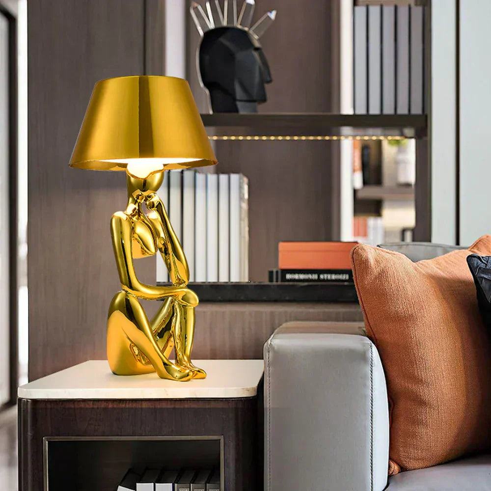 Arden designerlampa i guld på ett sidobord bredvid en soffa