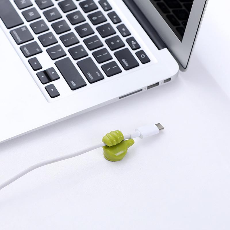 Grön självhäftande tumme upp kabelhållare på slät yta, effektivt organiserar kablar, passar dator- och USB-kablar.