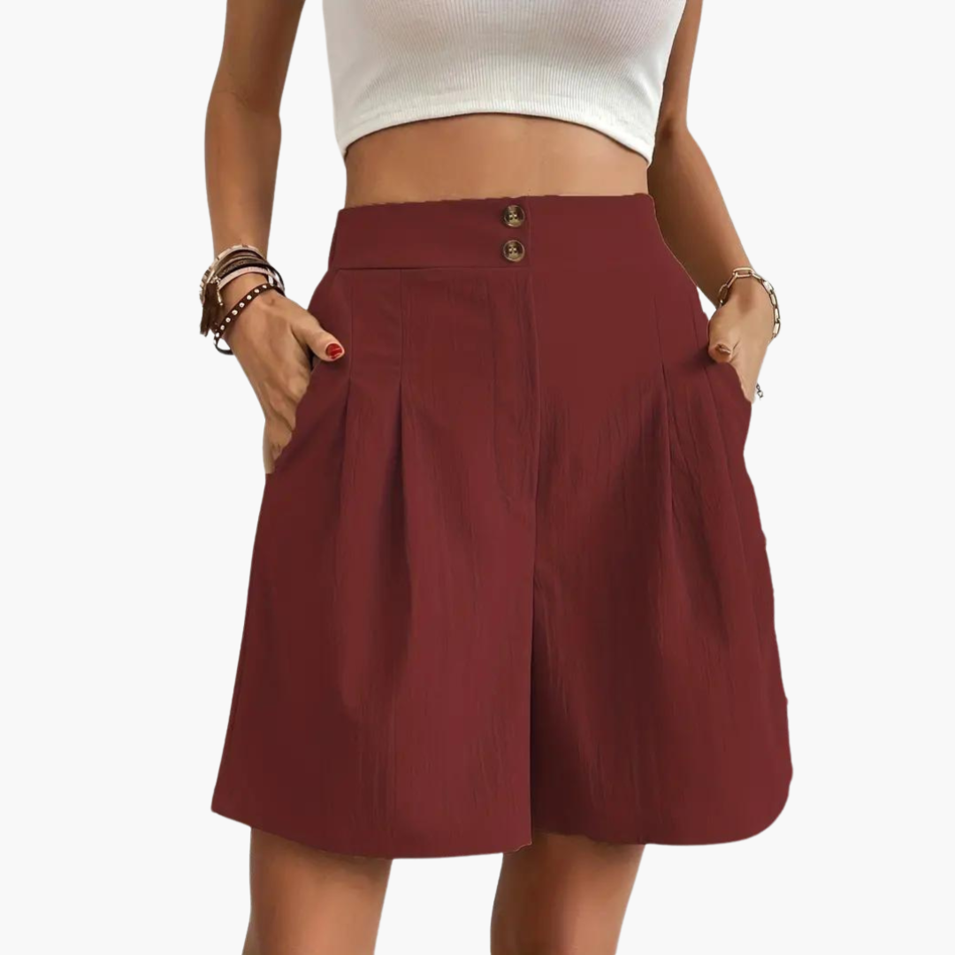 Modell bär den högmidjade plisserade minikjolen i en ledig sommaroutfit, framhäver silhuetten.