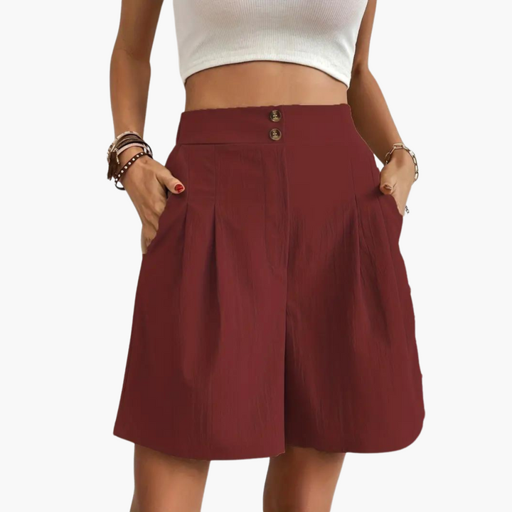 Modell bär den högmidjade plisserade minikjolen i en ledig sommaroutfit, framhäver silhuetten.