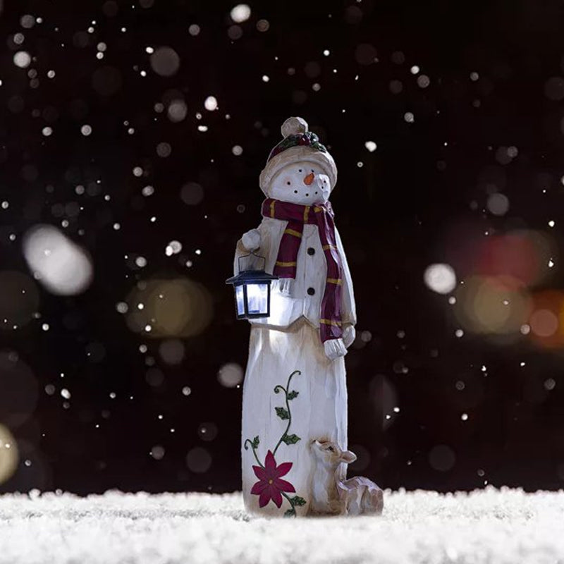"Handgjord snögubbe juldekoration med LED-lykta, snöhatt, röd halsduk i trädgård, för magisk julstämning i hemmet."