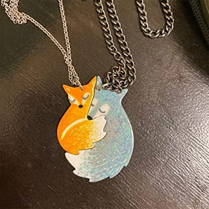 Handmålat parhalsband i stål med motiv av kramande räv och varg, perfekt för par och vänner.