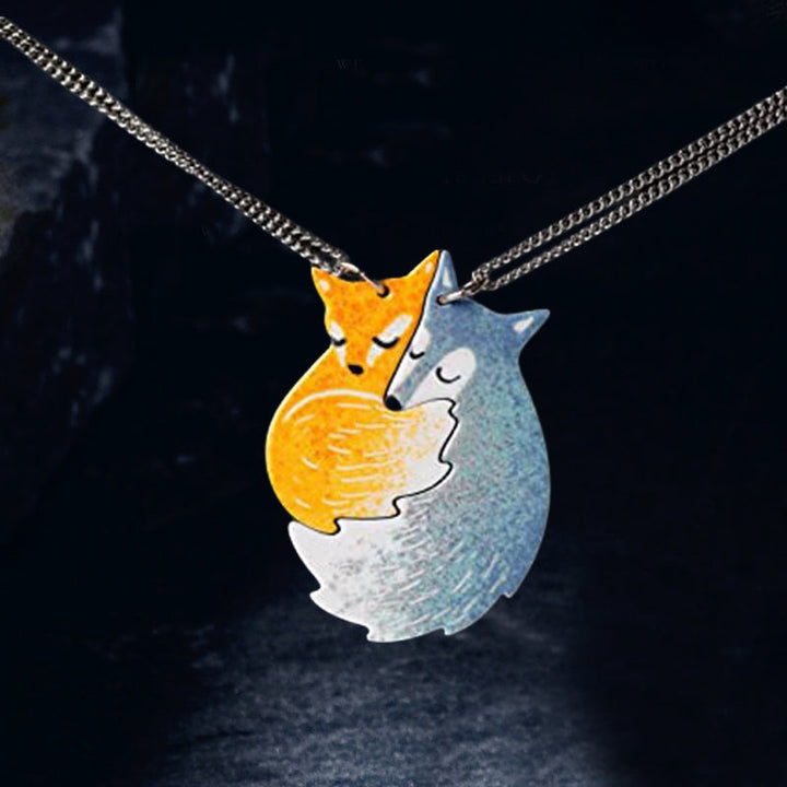 Handmålat parhalsband i stål med motiv av kramande räv och varg, perfekt för par och vänner.