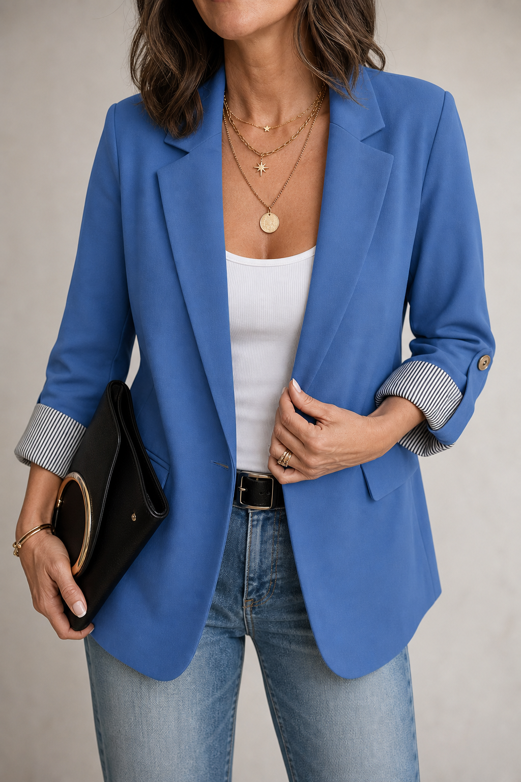 Kvinna i blå blazer med rollda ärmar som visar mönstrat foder, håller en svart clutch