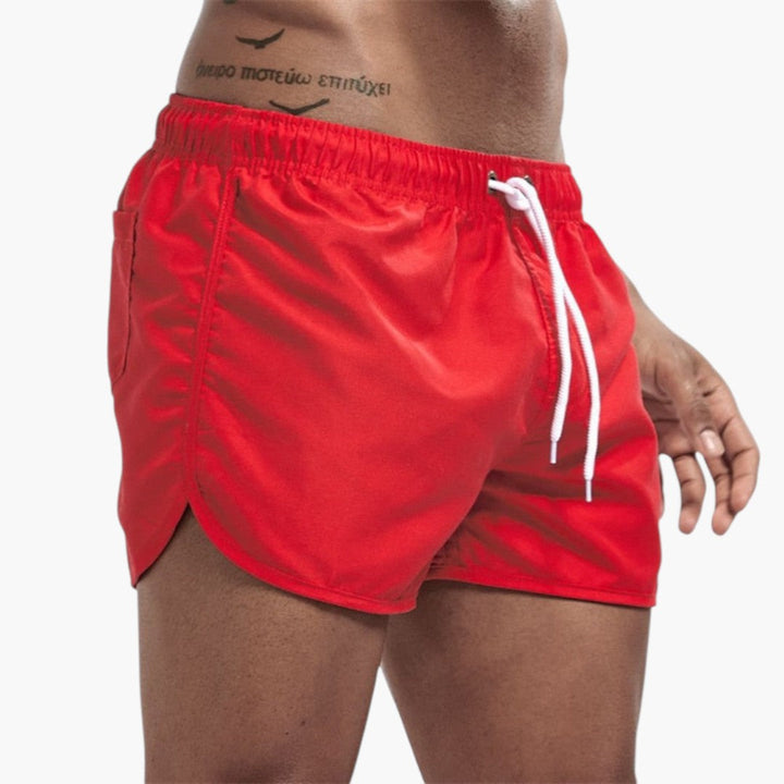 Herr i mångfärgade badshorts med dragsko, njuter vid poolen. Bekväma simshorts.