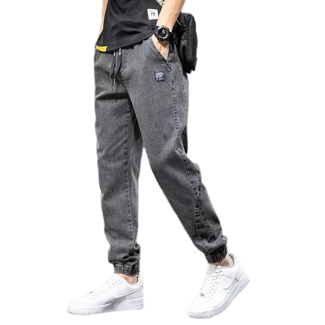 Man som bär gråsvarta jeans med avslappnad passform och vita sneakers