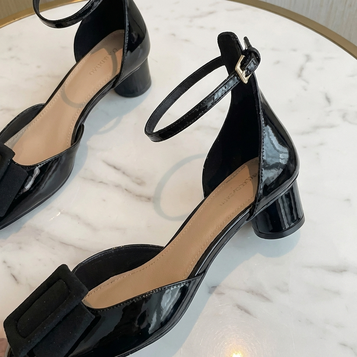 Närbild på eleganta svarta lackpumps med spänne på marmorbord