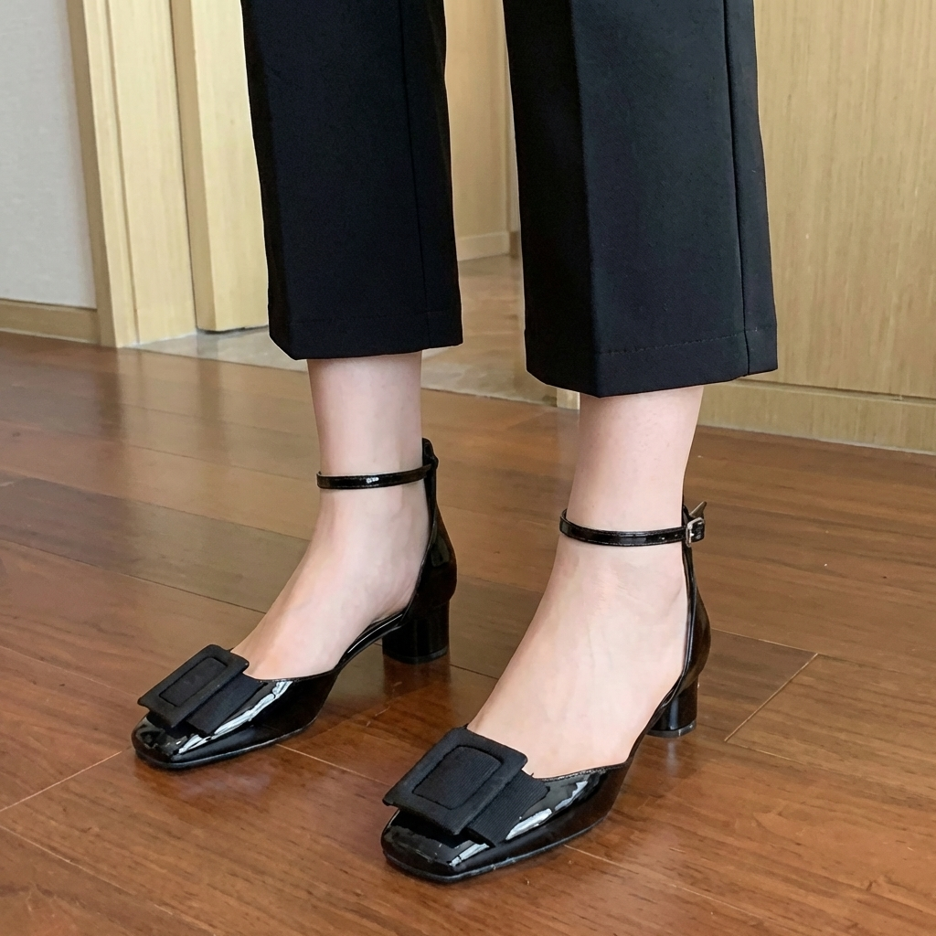Sandrine lackpumps i kolsvart färg med ankelrem på trägolv