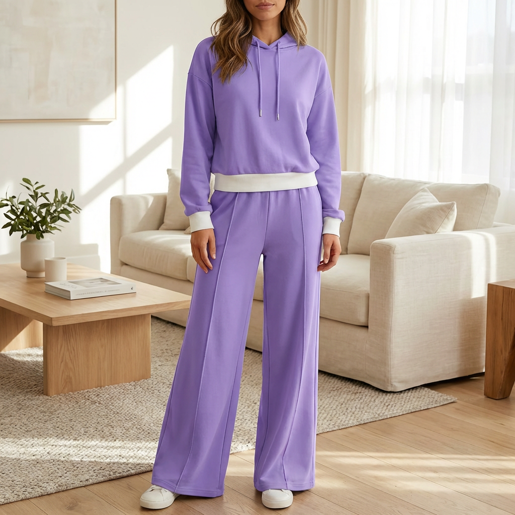 Kvinna i lila två-delat lounge-set med hoodie och matchande byxor stående i ett ljust vardagsrum